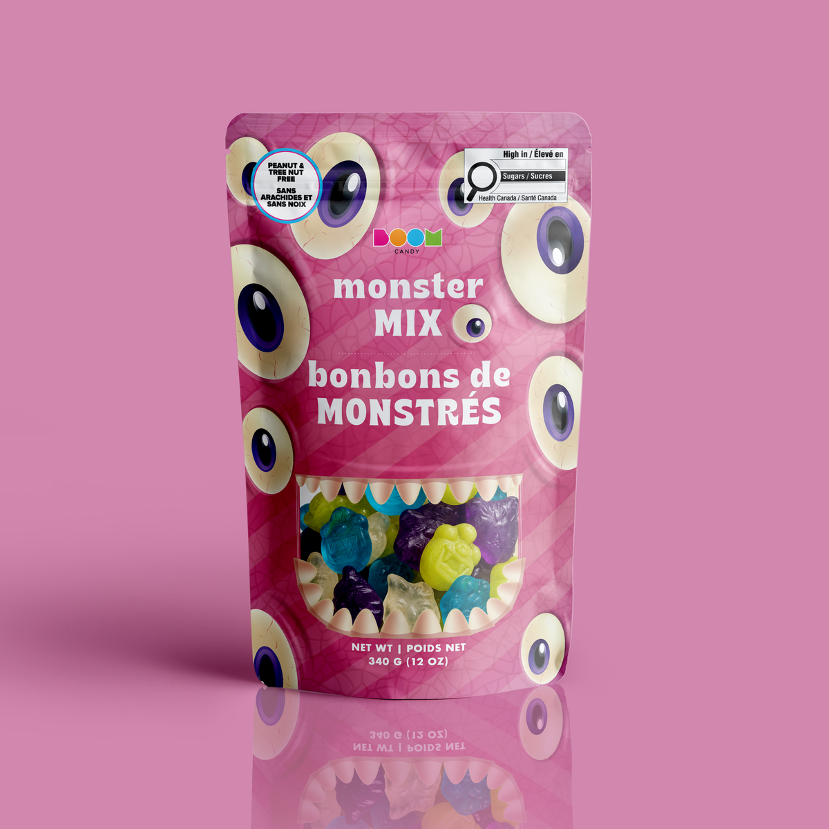 A bag of colourful monster gummies framed by a toothy mouth window in a pink eyeball monster Halloween pouch, certified 100% peanut and tree nut free.